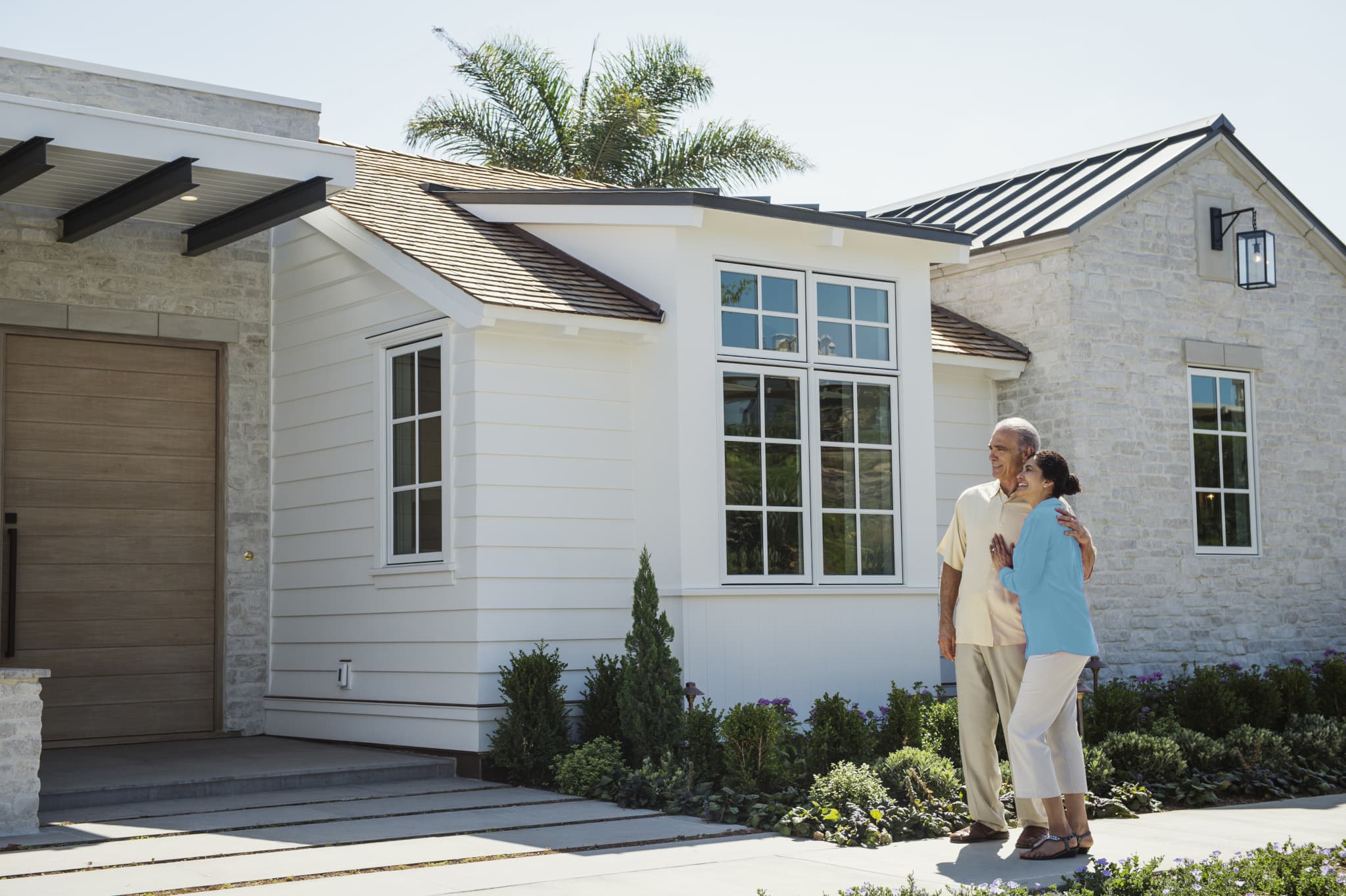 Couple embrace on the walkway outside their white and stone home