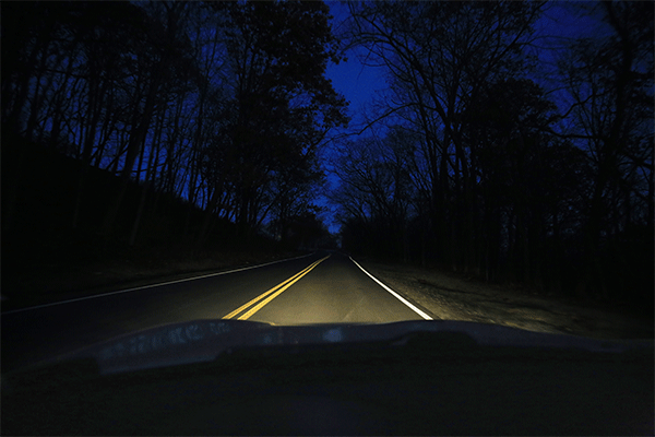 Car headlights as they change from parking to headlights to brights on a dark road at night.