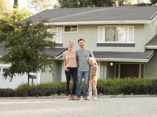Mother, father and child standing in front of their home.