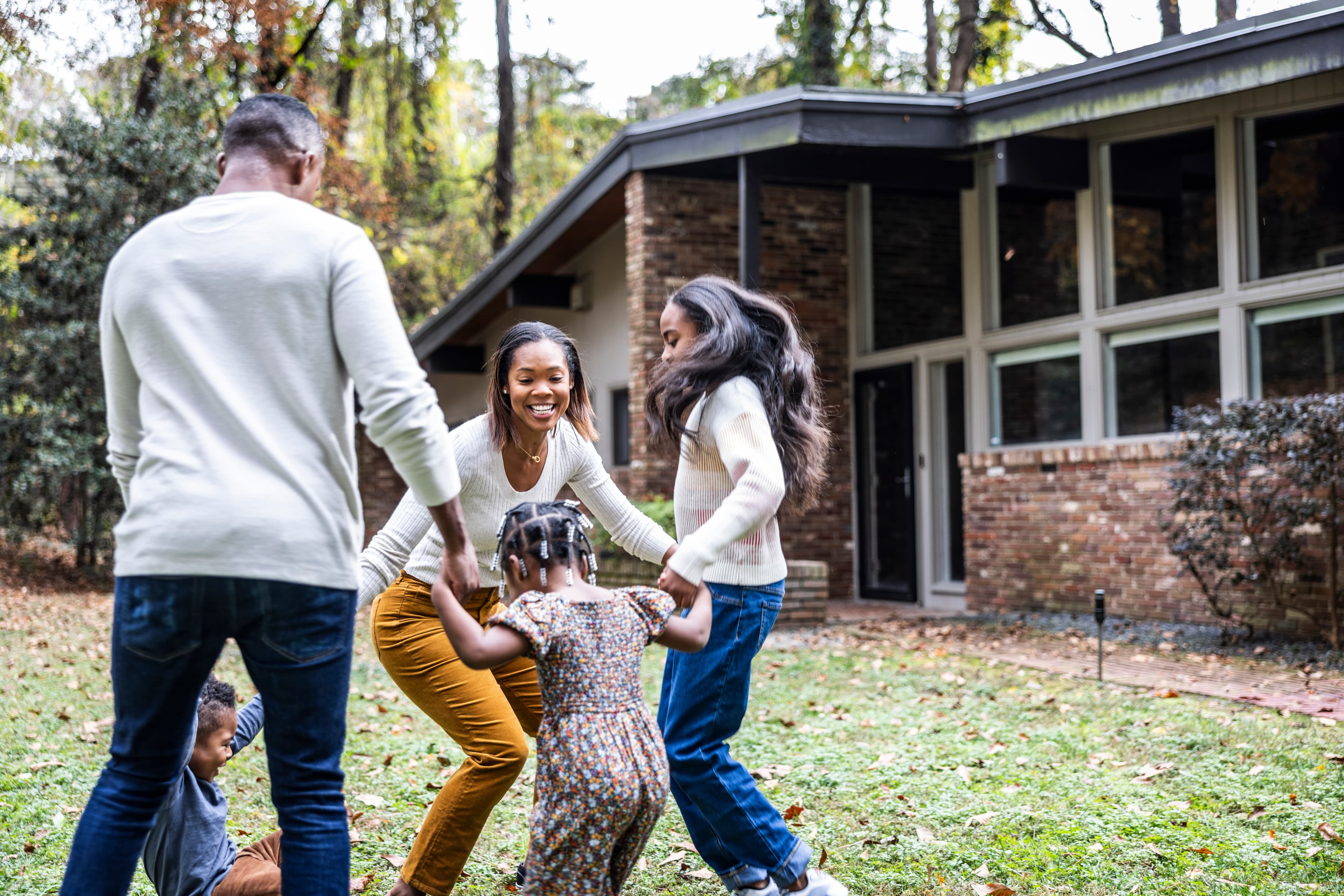 A family plays together on the lawn outside their brick home