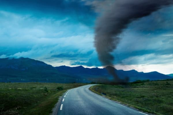 Tornado about to cross a rural road with mountains behind it.