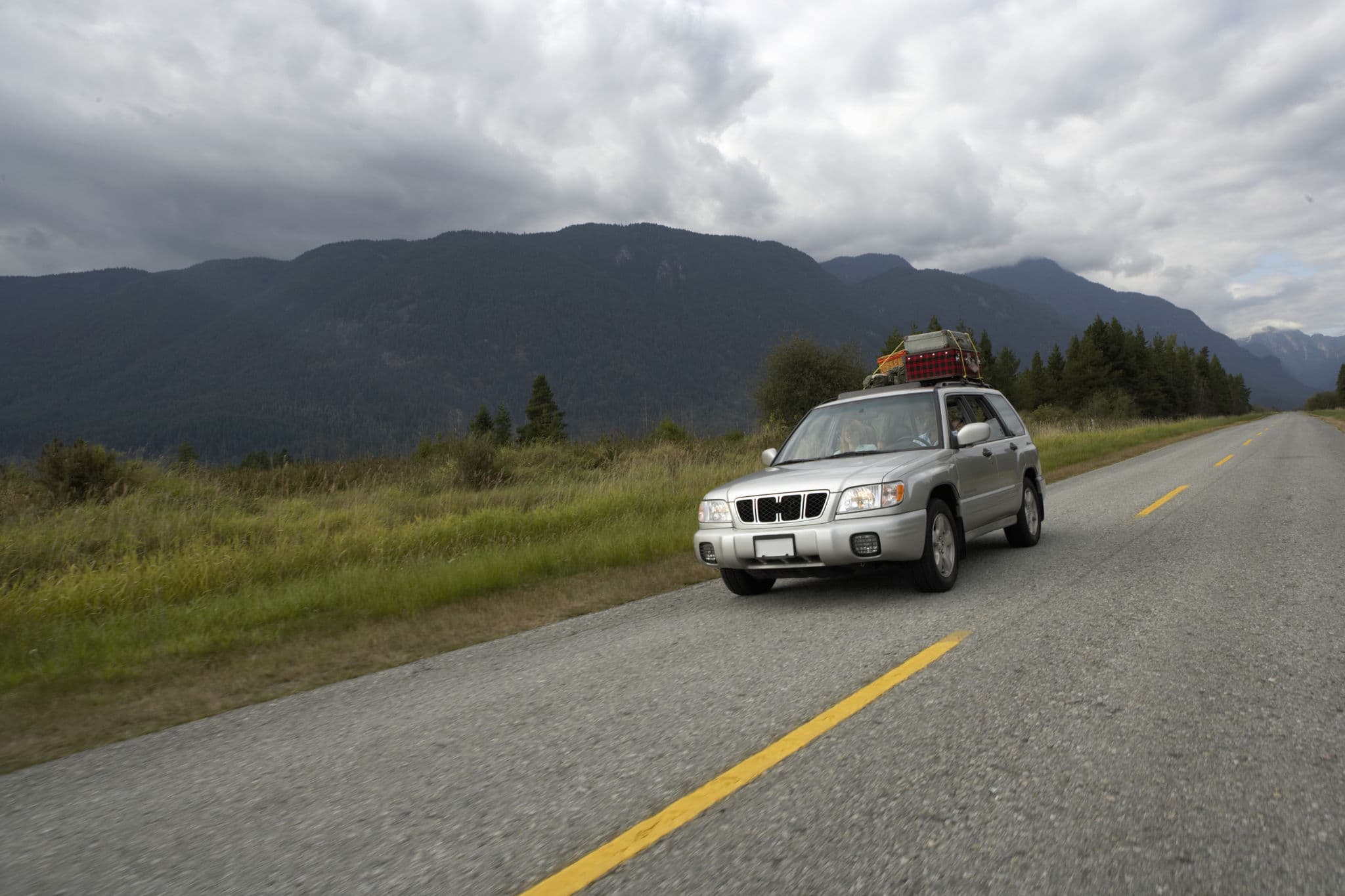 Older silver SUV with a loaded roof rack drives along a mountain road, a typical vehicle for car insurance for older cars