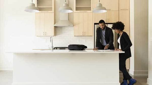 A couple standing in their kitchen, reading a document and smiling.