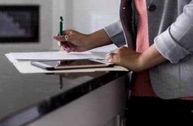 Woman filling out paperwork while standing at a kitchen island.