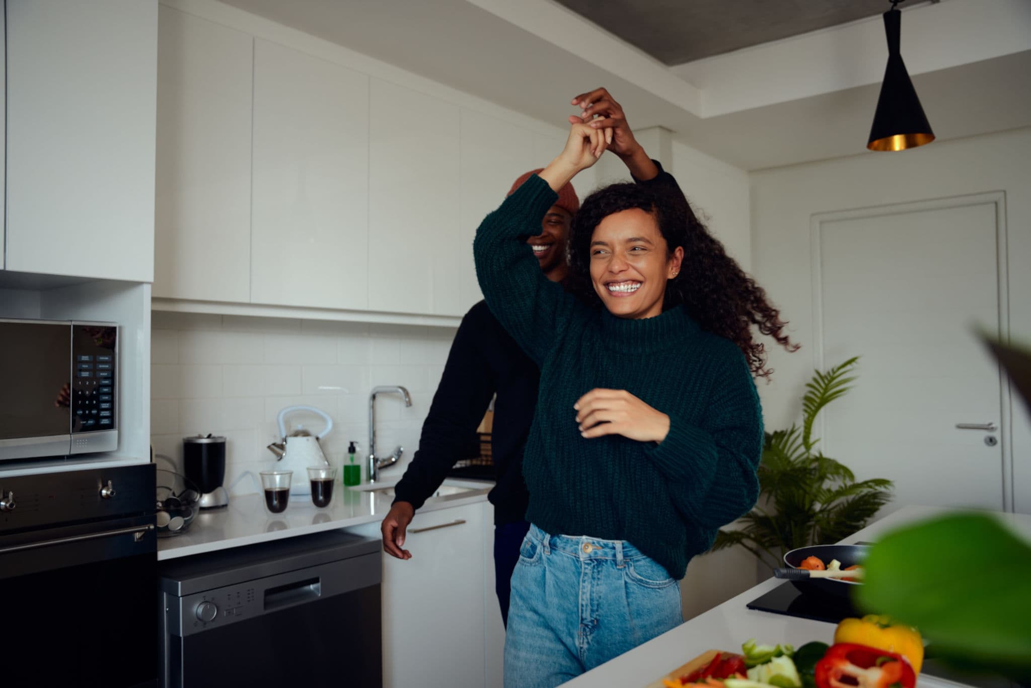 Couple laugh and dance together in a bright kitchen while cooking