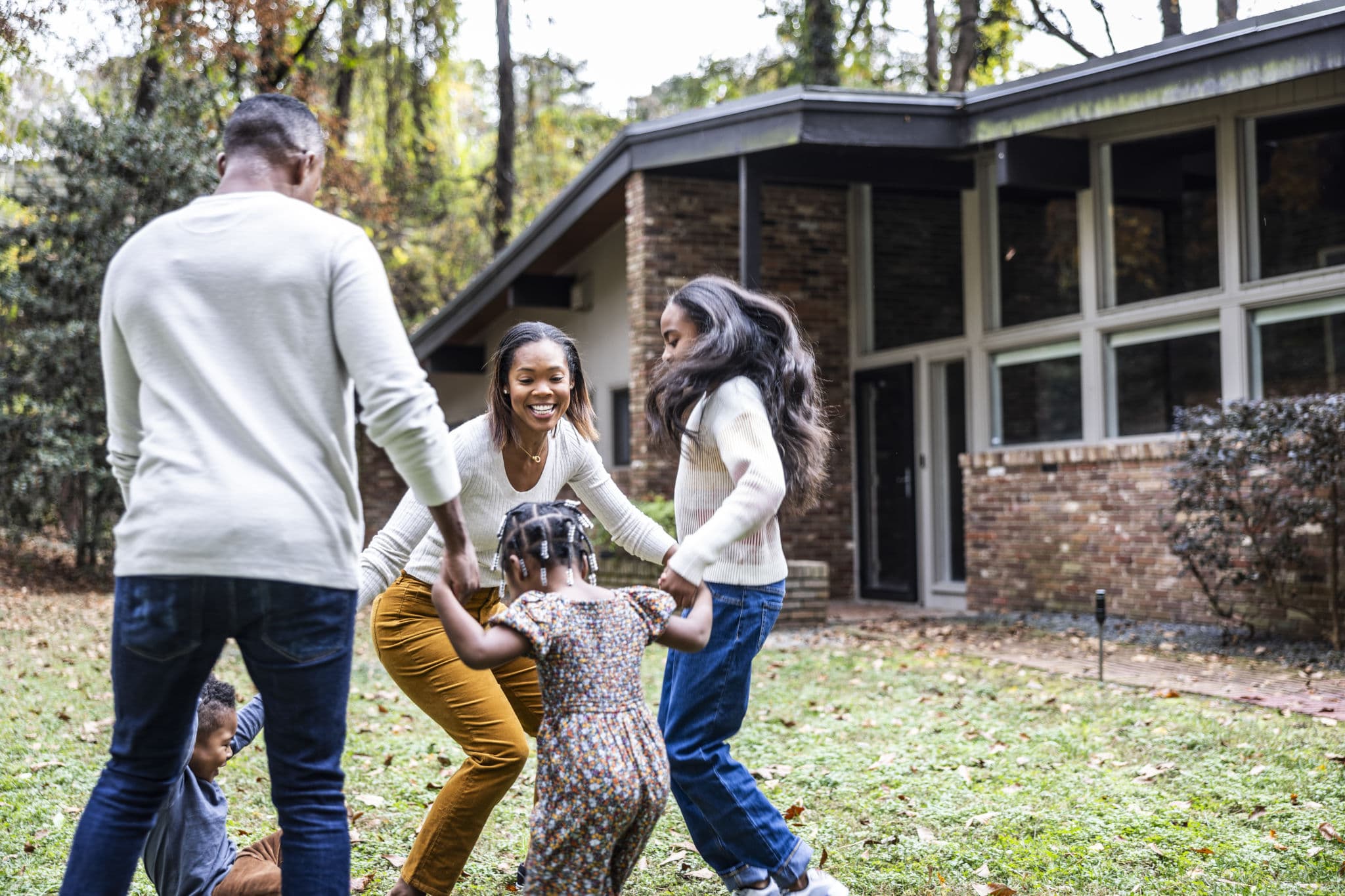 A family plays together on the lawn outside their brick home