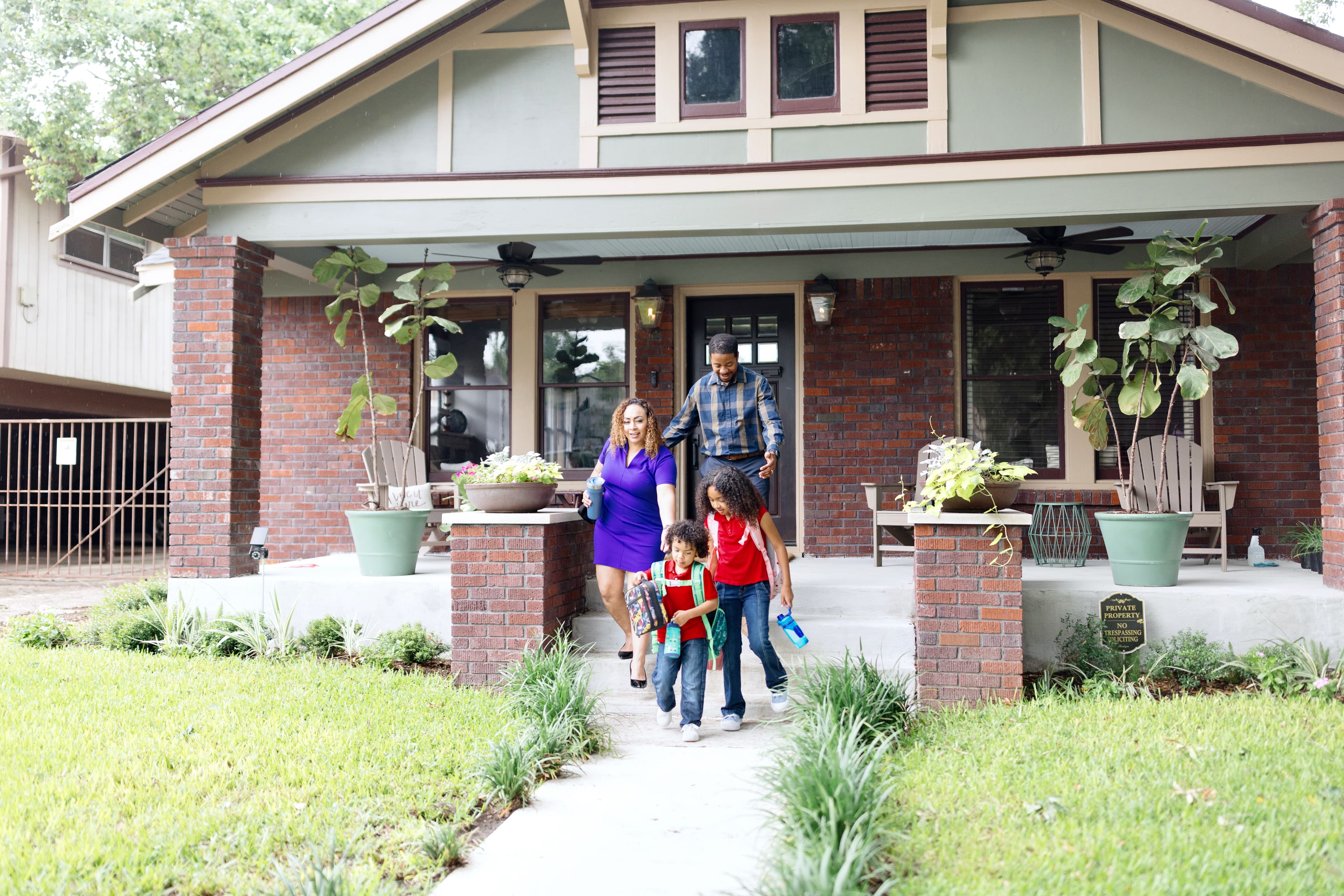 Parents and two kids walk out the front door of an older brick bungalow