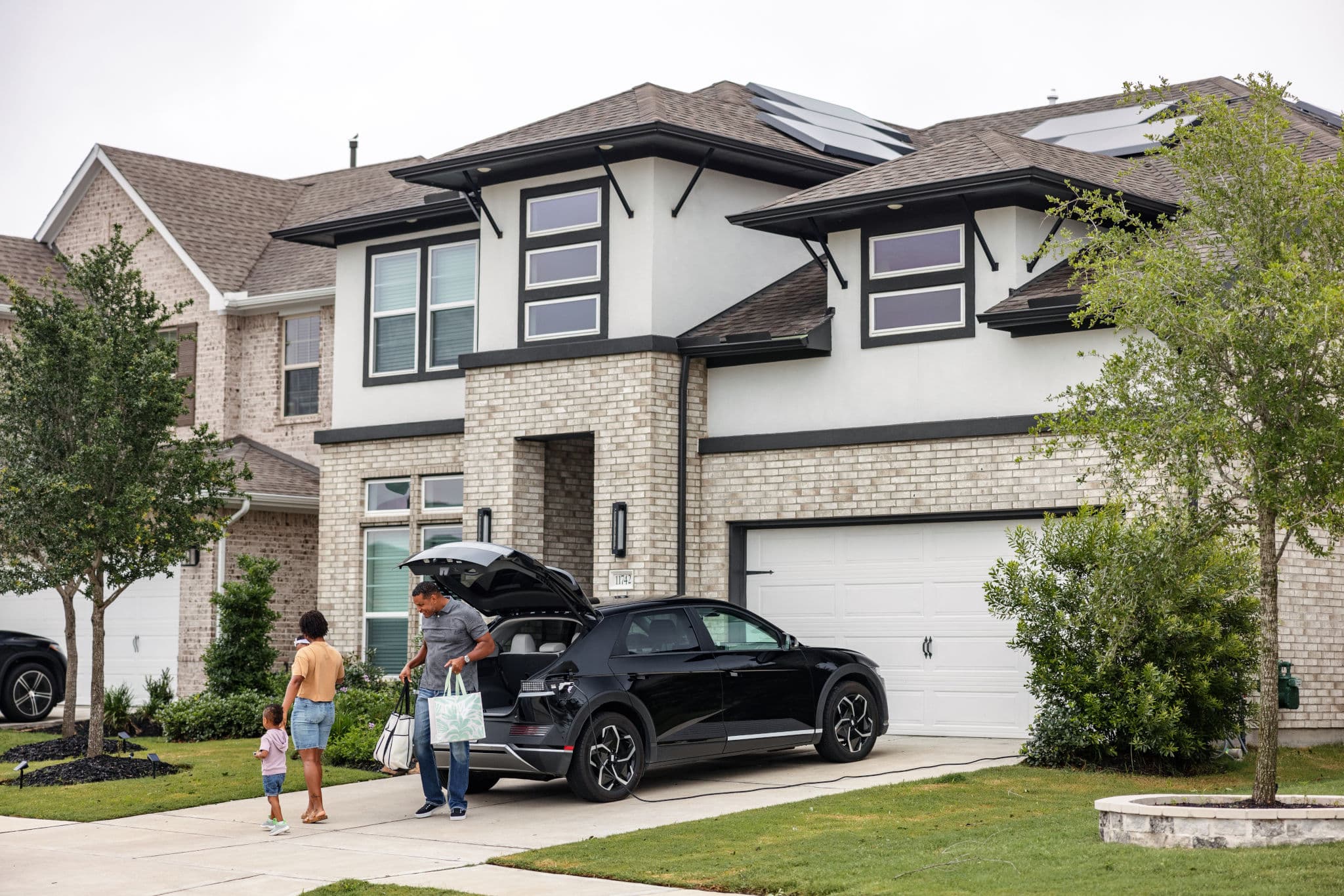 A man, a woman and a toddler unload bags from a black SUV in front of their home