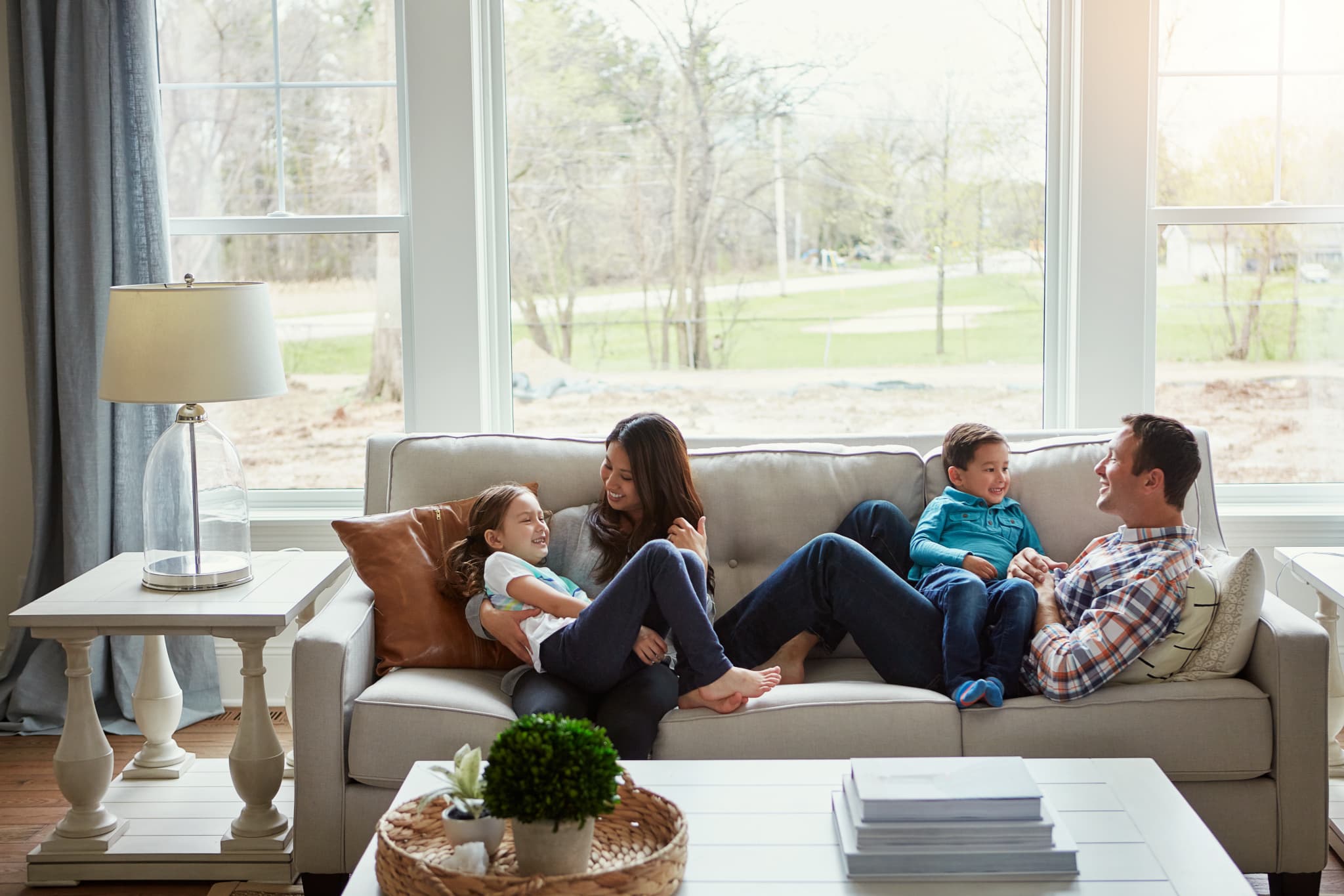 A family of four laughs together on a couch in a bright living room