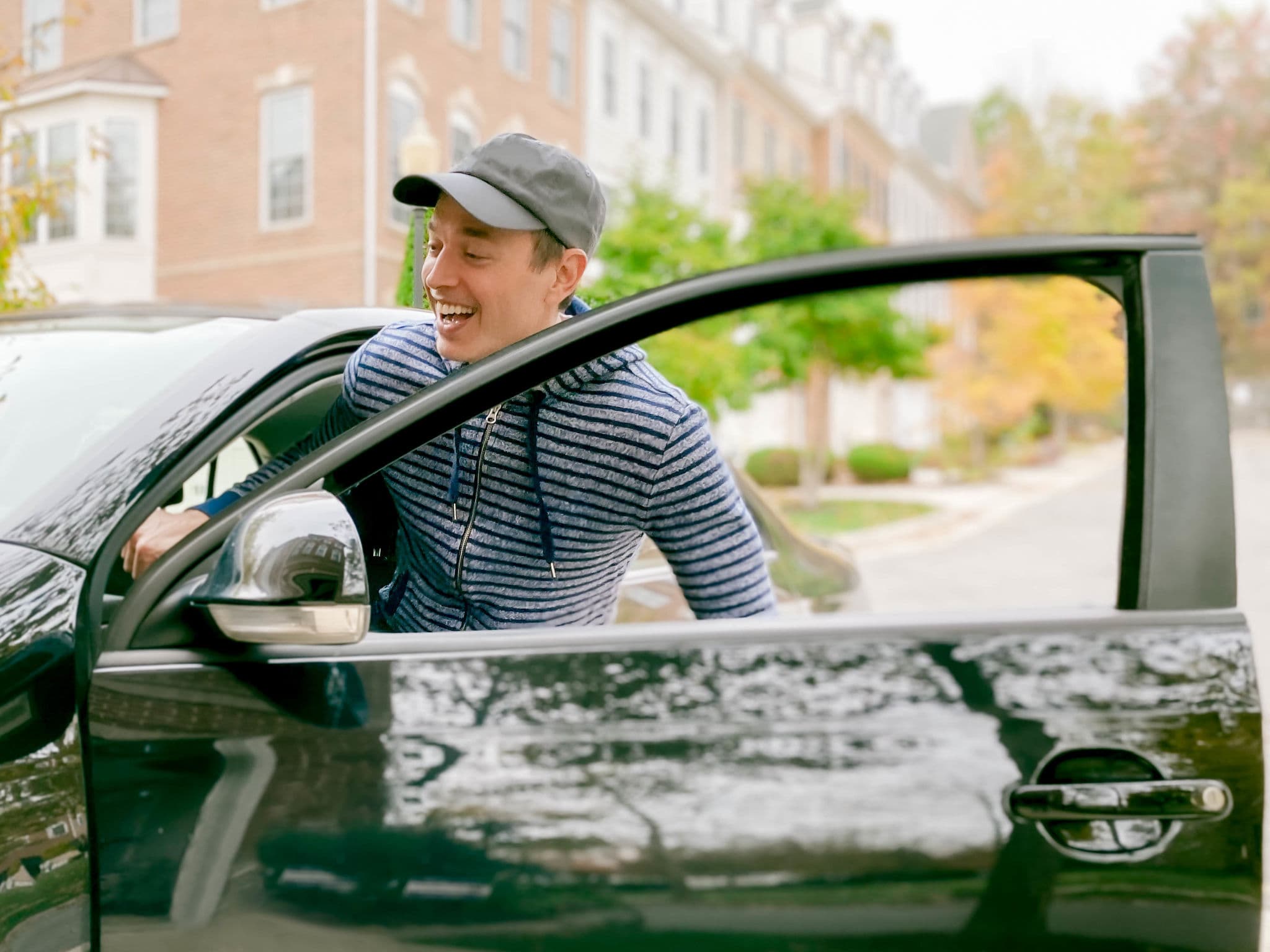 Smiling driver opens the door of his car on a quiet street, a milestone moment once your car is paid off