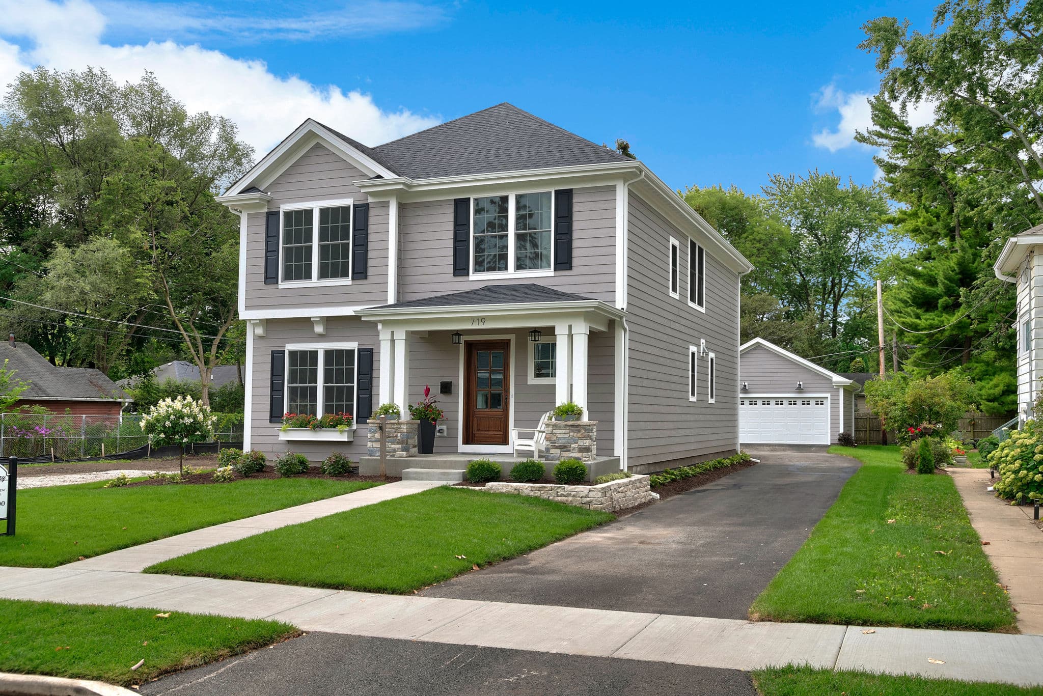 Two-story unoccupied house with a covered porch, an empty driveway and a detached garage