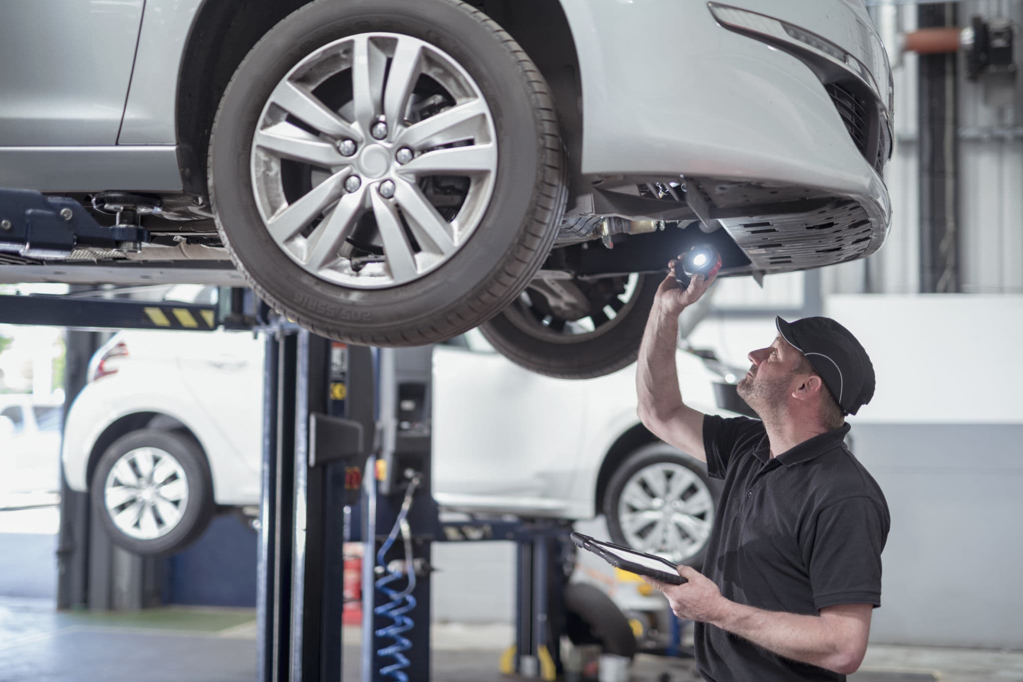 Mechanic inspects the underside of a car on a lift, to show parts and labor cost that may impact your car insurance rate
