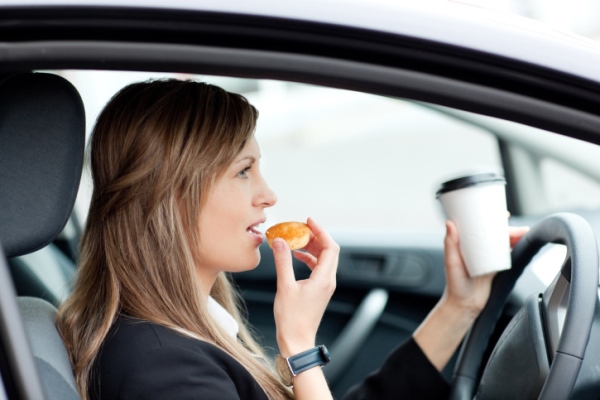 woman driving while holding coffee and donut