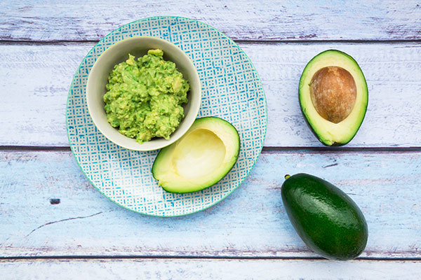 Bowl of Guacamole and whole and sliced avocados on light blue wood