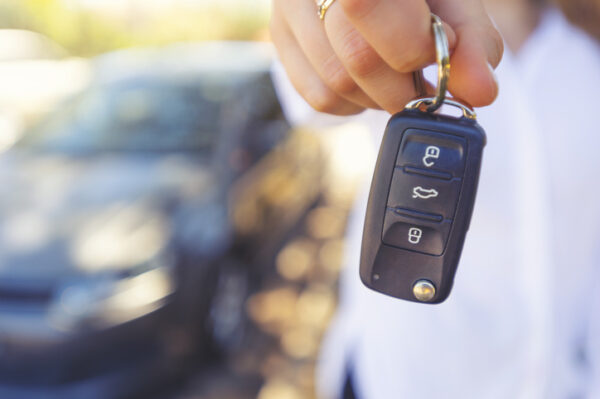Female car salesperson handing over the new car keys. There is a new car behind her out of focus. Close up with Copy space