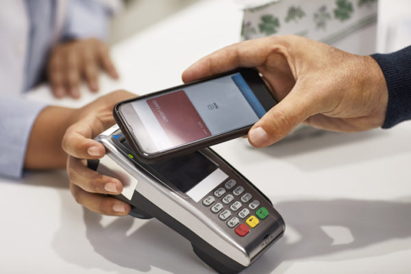Cropped image of man using contactless payment in medical store. Hands of cashier and customer holding technologies. They are at checkout counter.