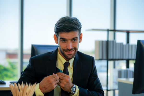 portrait of caucasian young businessman wearing suit with the mobile phone and computer looked at the camera to have the teleconference with the office meeting