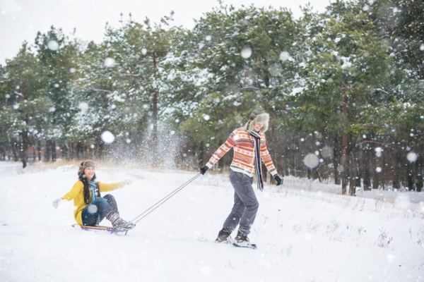 man pulling woman on sled through snow