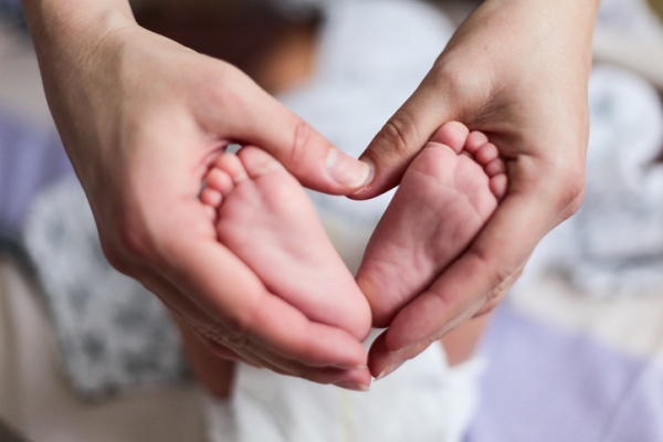 Parents making a heart shape with their hands around their newborn baby's feet.