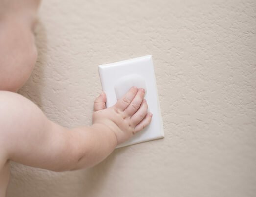 Baby trying to pull off a plastic outlet cover.