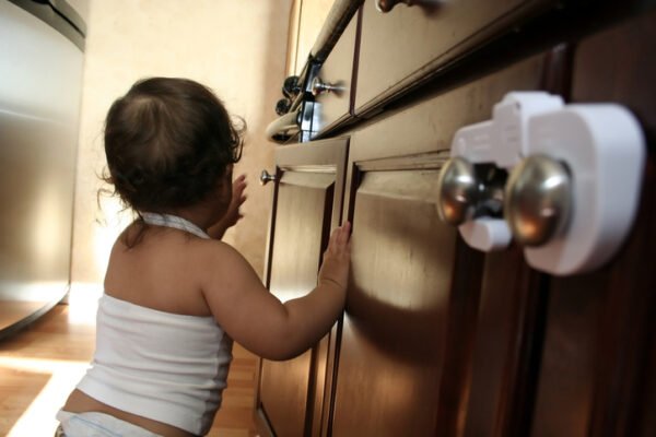 Baby walking next to kitchen cupboards with baby locks installed.