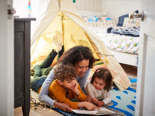 Mom reading book to her children inside a play tent in the children's bedroom.