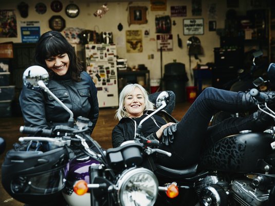 Two women taking a break from driving while sitting on their motorcycles.