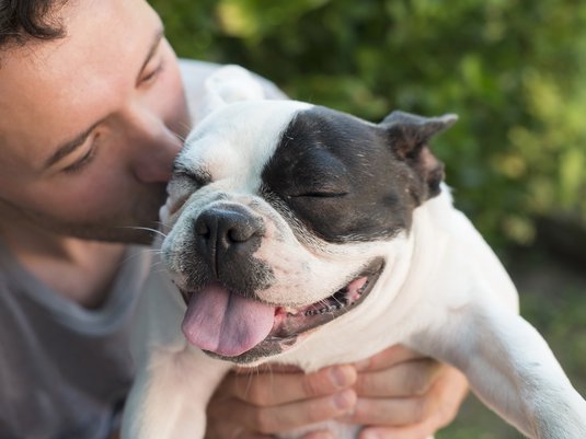 Man holding his dog up and kissing it on the head.