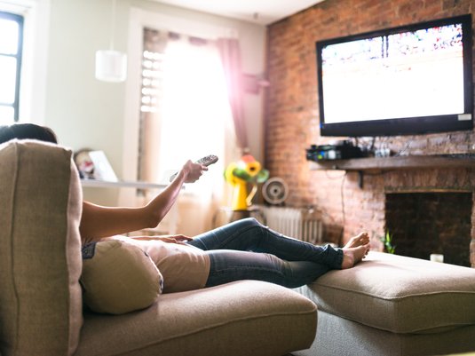 A person sitting in the living room of their rental, watching tv.