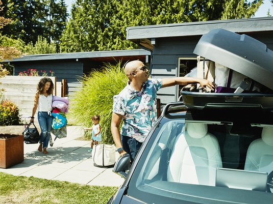 Family packing their car roof rack with luggage to prepare for a trip.