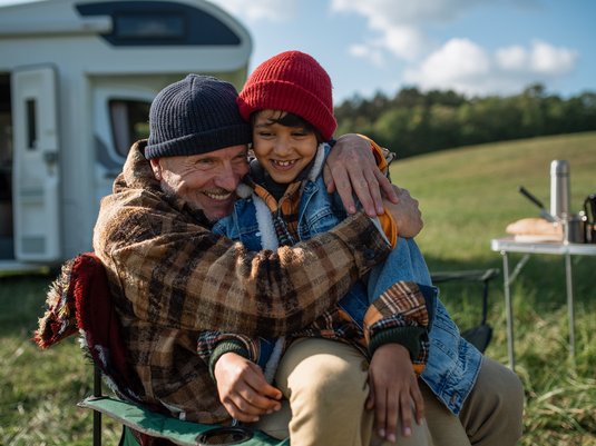 Grandfather hugging his grandchild on camping trip in front of their rv.