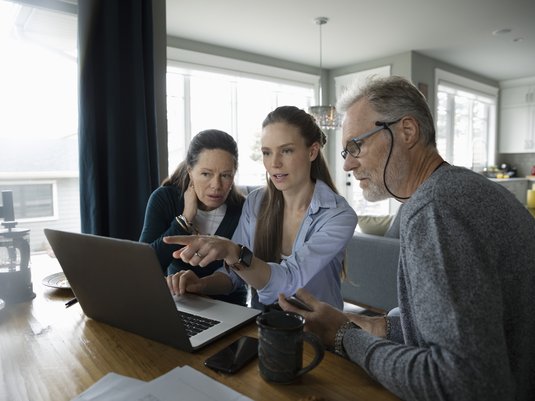 Adult woman showing her parents something on a laptop.
