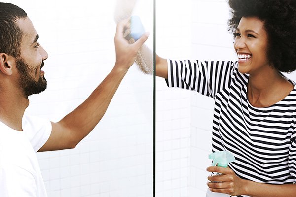 Man and woman cleaning opposite sides of a glass panel while smiling and laughing at each other.
