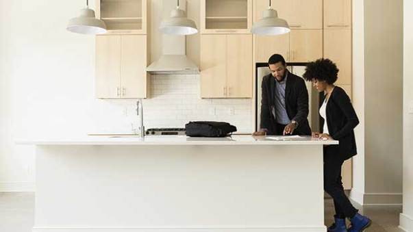 A couple standing in their kitchen, reading a document and smiling.