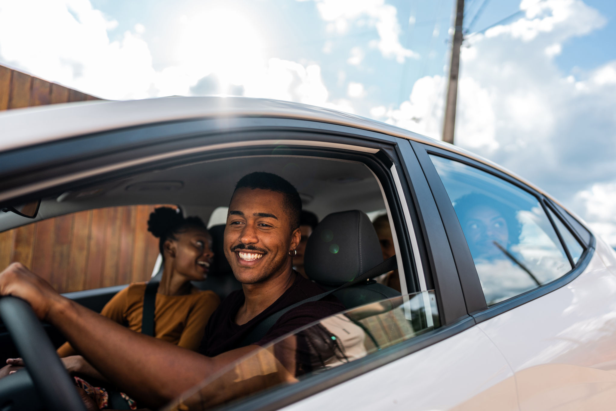 smiling driver with passengers in a car, illustrating whether insurance covers the car or the driver