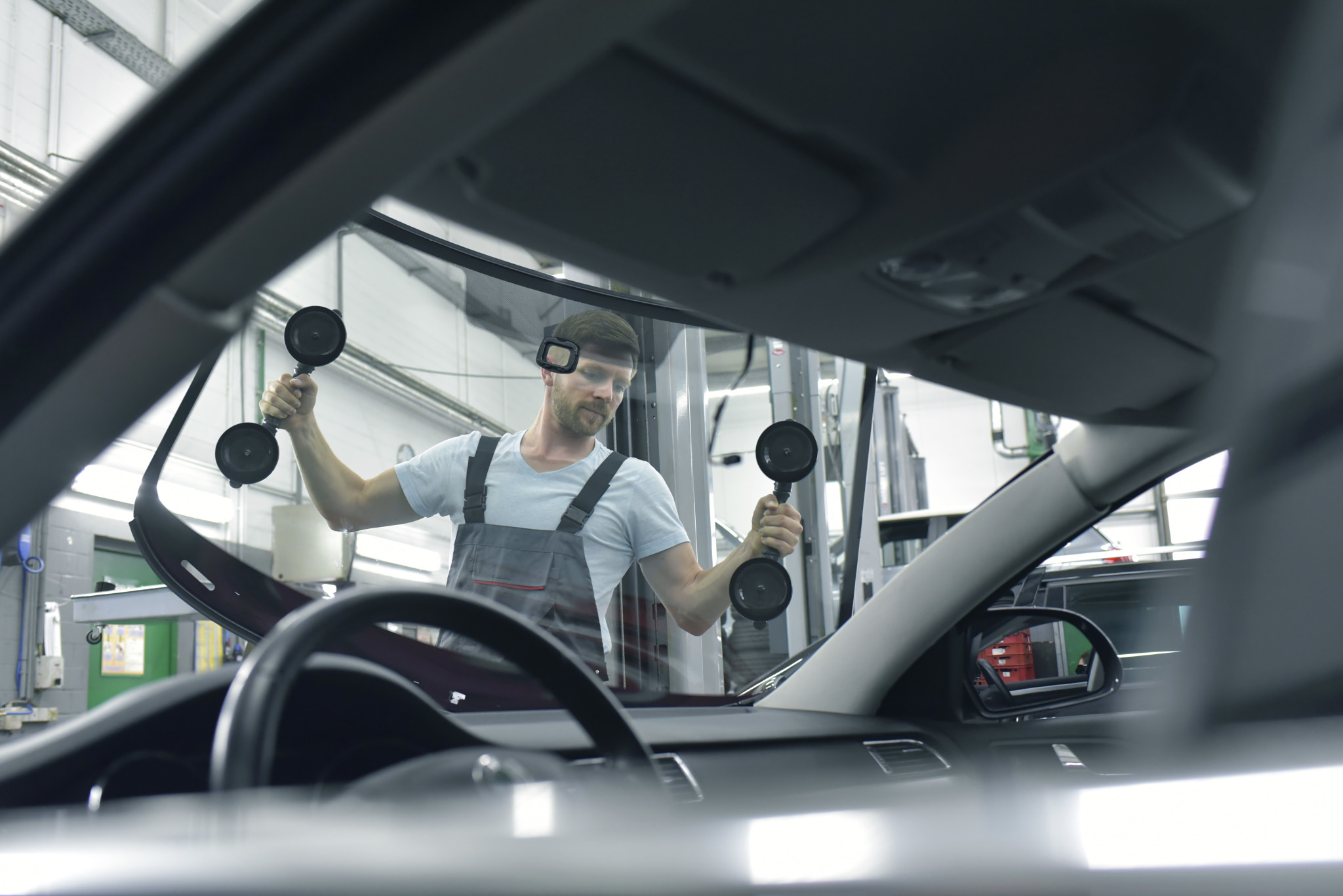 Technician installs a replacement windshield using suction-cup handles in an auto glass repair shop