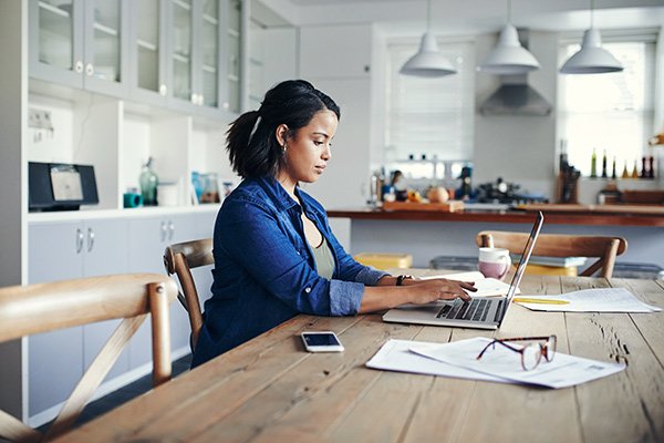 Woman working on her laptop while seated at her kitchen table.