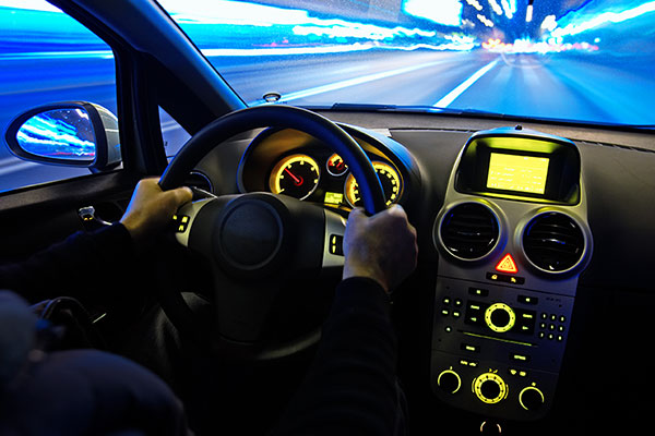 Picture of a man driving a car at night, taken from the backseat of the car.
