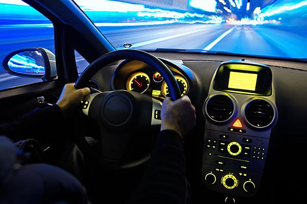 Picture of a man driving a car at night, taken from the backseat of the car.