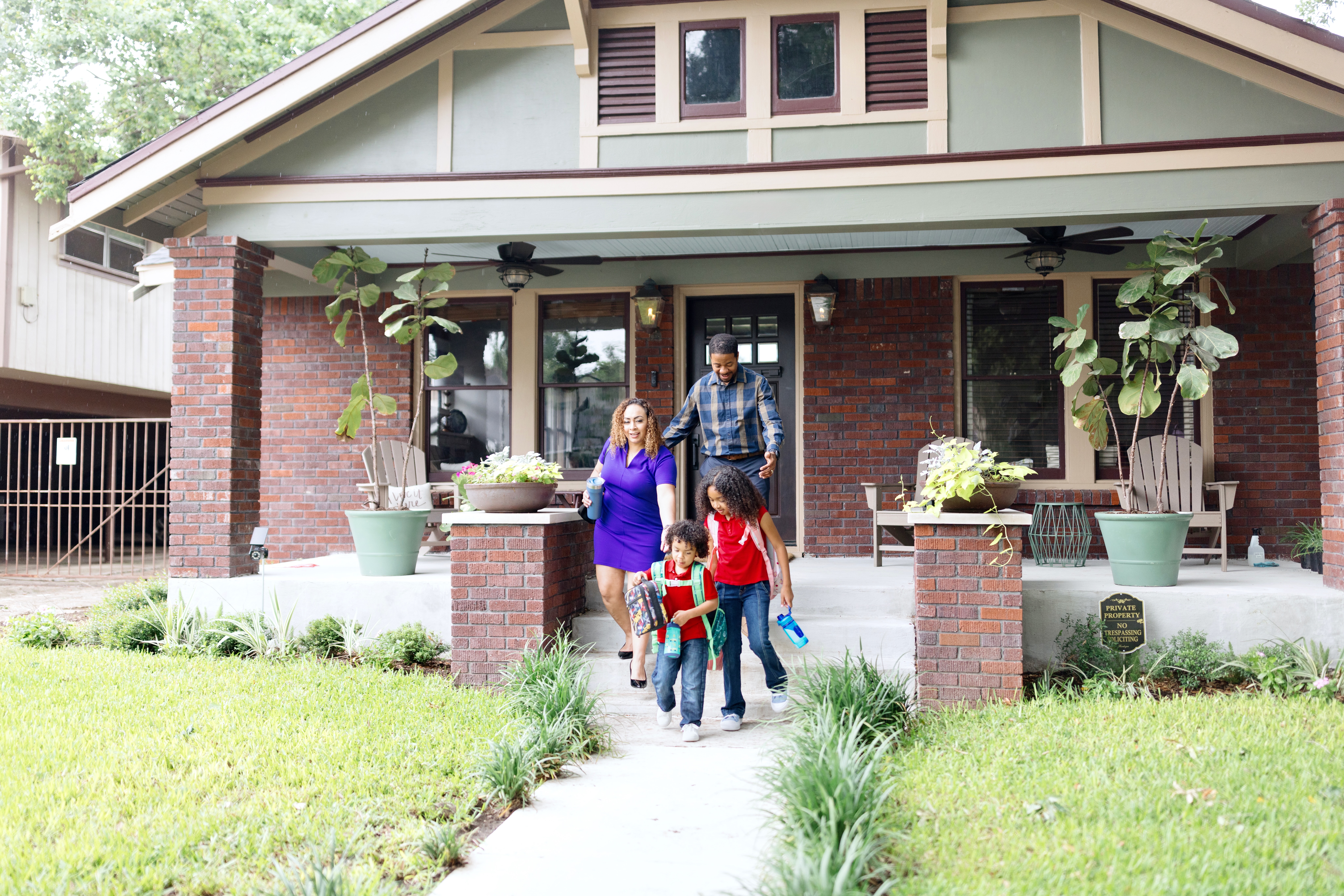 Parents and two kids walk out the front door of an older brick bungalow