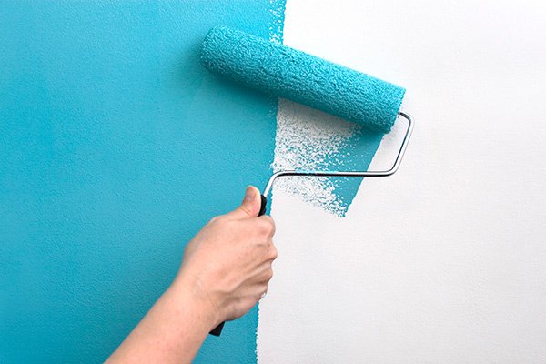 Paint roller applying turquoise paint to a white wall.