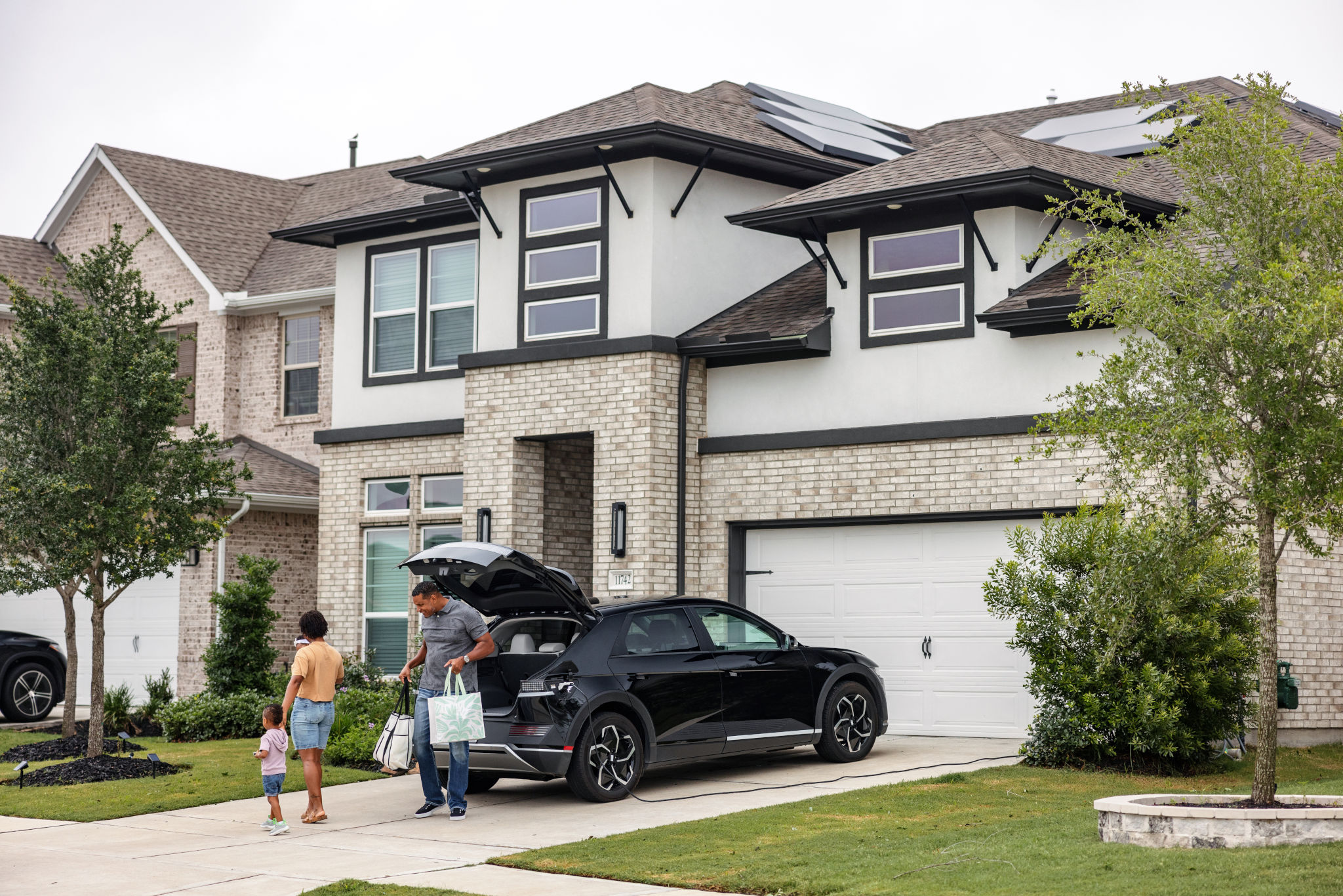 A man, a woman and a toddler unload bags from a black SUV in front of their home