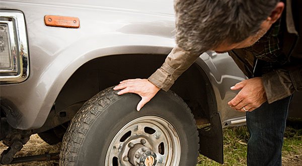 Man bent over next to car as he inspects the tire.
