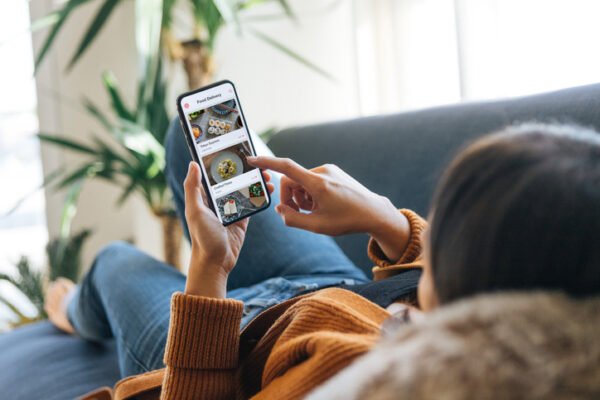 Woman lying on the couch and looking at her phone screen that shows different food options.