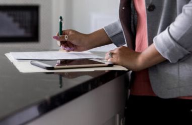 Woman filling out paperwork while standing at a kitchen island.