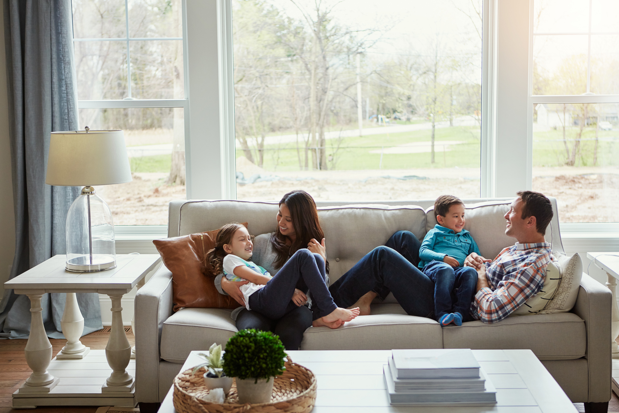 A family of four laughs together on a couch in a bright living room