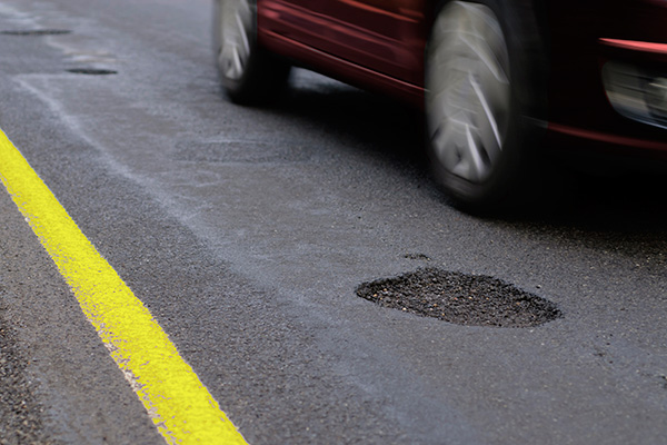 A car driving next to several potholes in a street.