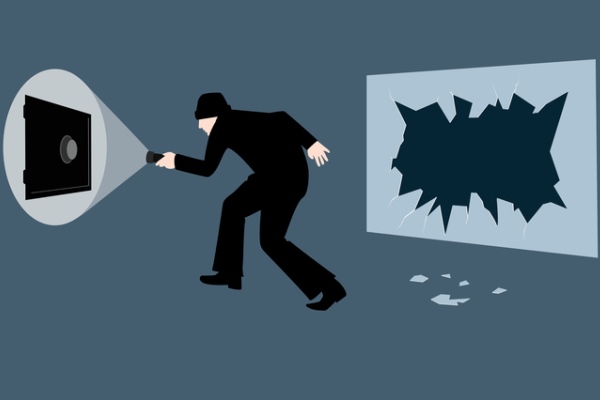 Burglar creeping across a dark and empty room to a wall safe, with a broken window behind him.