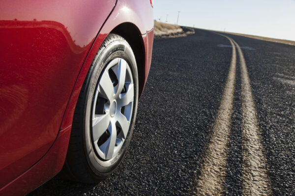Close up of a rear tire of a red car as it drives down a street.