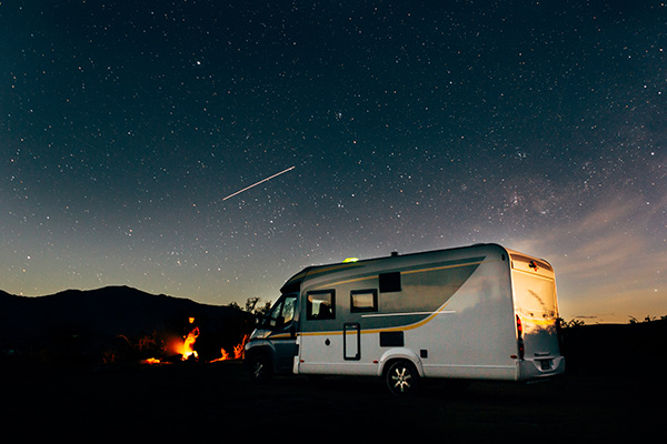 RV camping in the desert at night with night sky and a meteor in background.